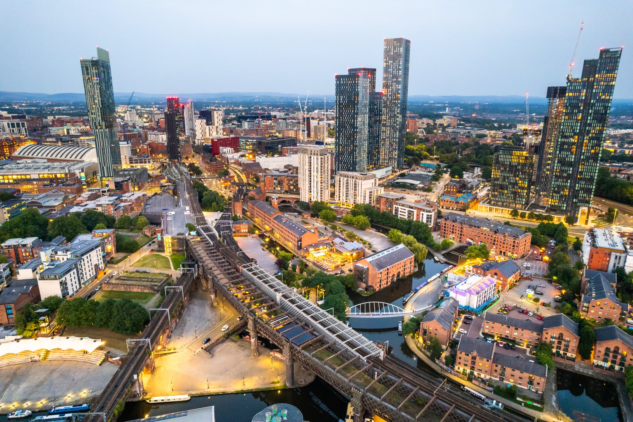 Manchester United Kingdom aerial shot of modern buildings with lots of counstruction in the central area of the city with historic canals and railways in the foreground by night
