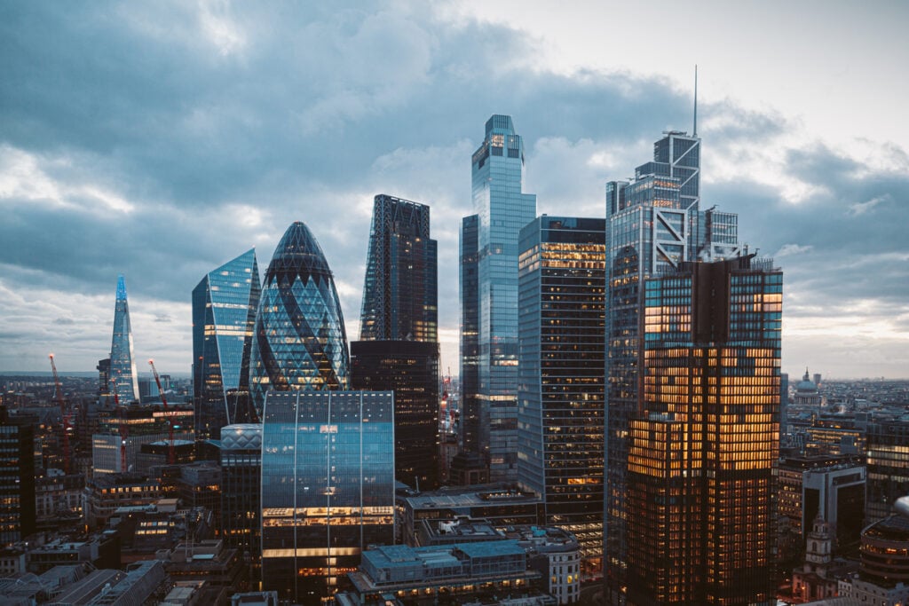 Aerial panoramic view of The City of London cityscape skyline with metropole financial district modern skyscrapers after sunset on night with illuminated buildings and cloudy sky in London, UK